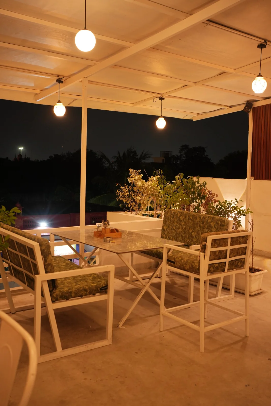 Tables, chairs, plants and warm hanging lights in the cafe seating area. Nasha Chai Sutra, SFS Mansarovar Jaipur.