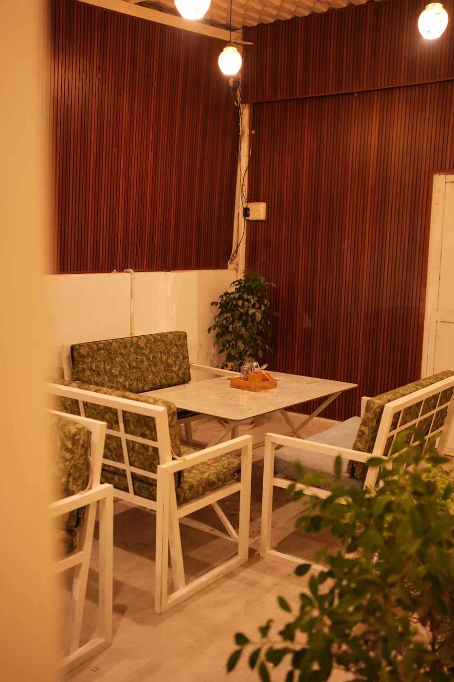 A two-chair cafe table beside the wall and plants. Nasha Chai Sutra, SFS Mansarovar Jaipur.