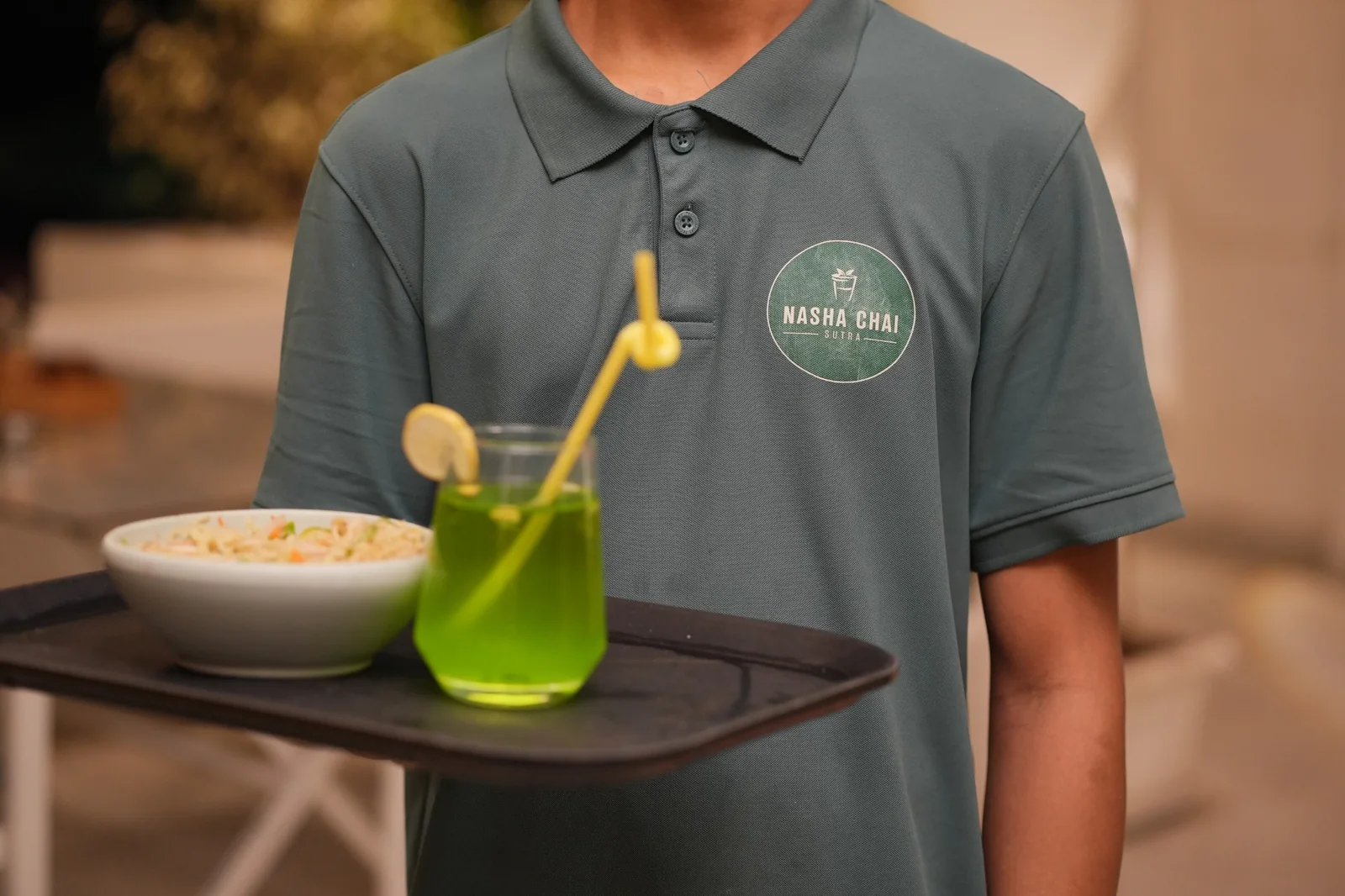 An NCS team member carrying a tray with pasta and a green drink. Nasha Chai Sutra, SFS Mansarovar Jaipur.